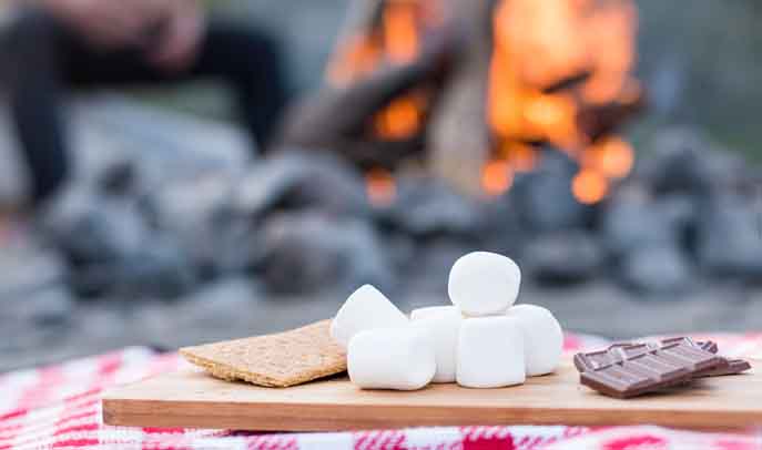 Traditional smores ready to eat next to a warm glowing fire