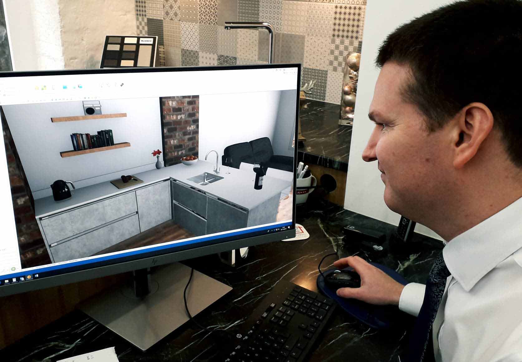 A man sitting at a computer with a computer generated image of a kitchen on the screen