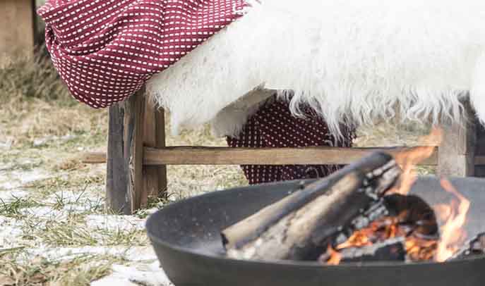 Firepit with soft, white textured sheepskin rugs and throws for all year round cosy warmth outdoors 