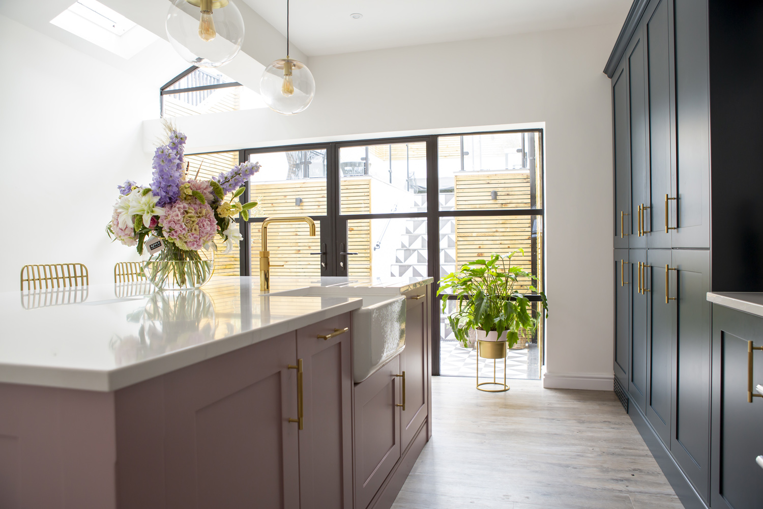 Stoneham Kitchen with a dusky pink kitchen island and dark blue cabinets looking out to a beautiful garden