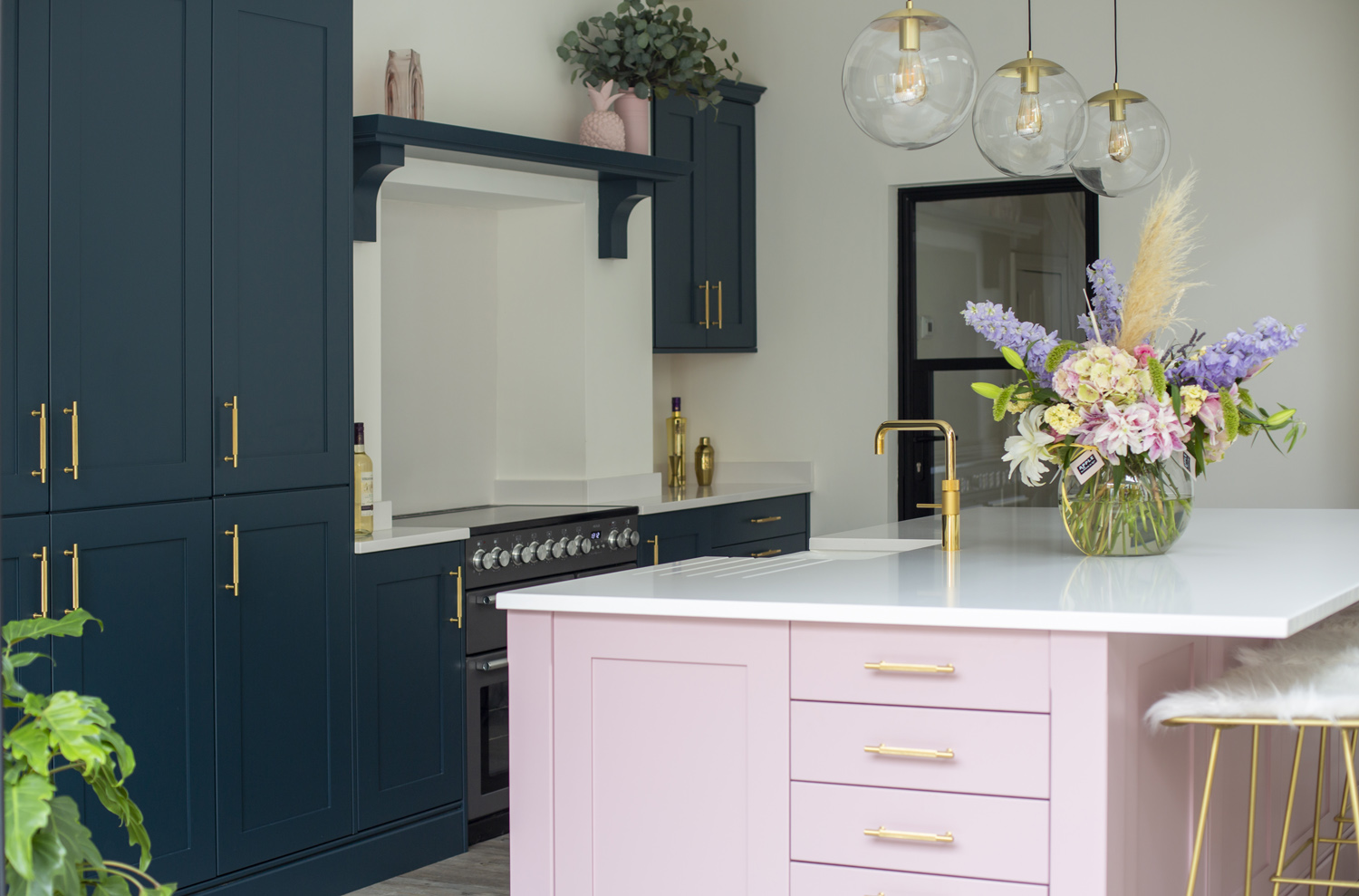 Stoneham Kitchen with a dusky pink kitchen island, dark blue cabinetry and gold lights and accessories
