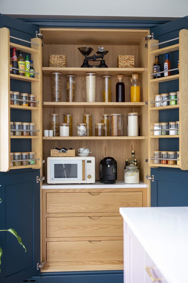A wide open pantry with oak shelves, the shelves are full of food and house small electrical appliances too.